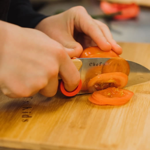 Een kind snijd groente op een chef-kids snijplank met een opinel mes waarmeer kinderen koken op de BSO